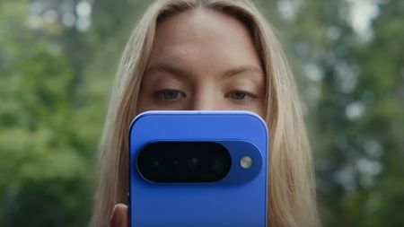 A woman looking at a blue Google Pixel 10 phone